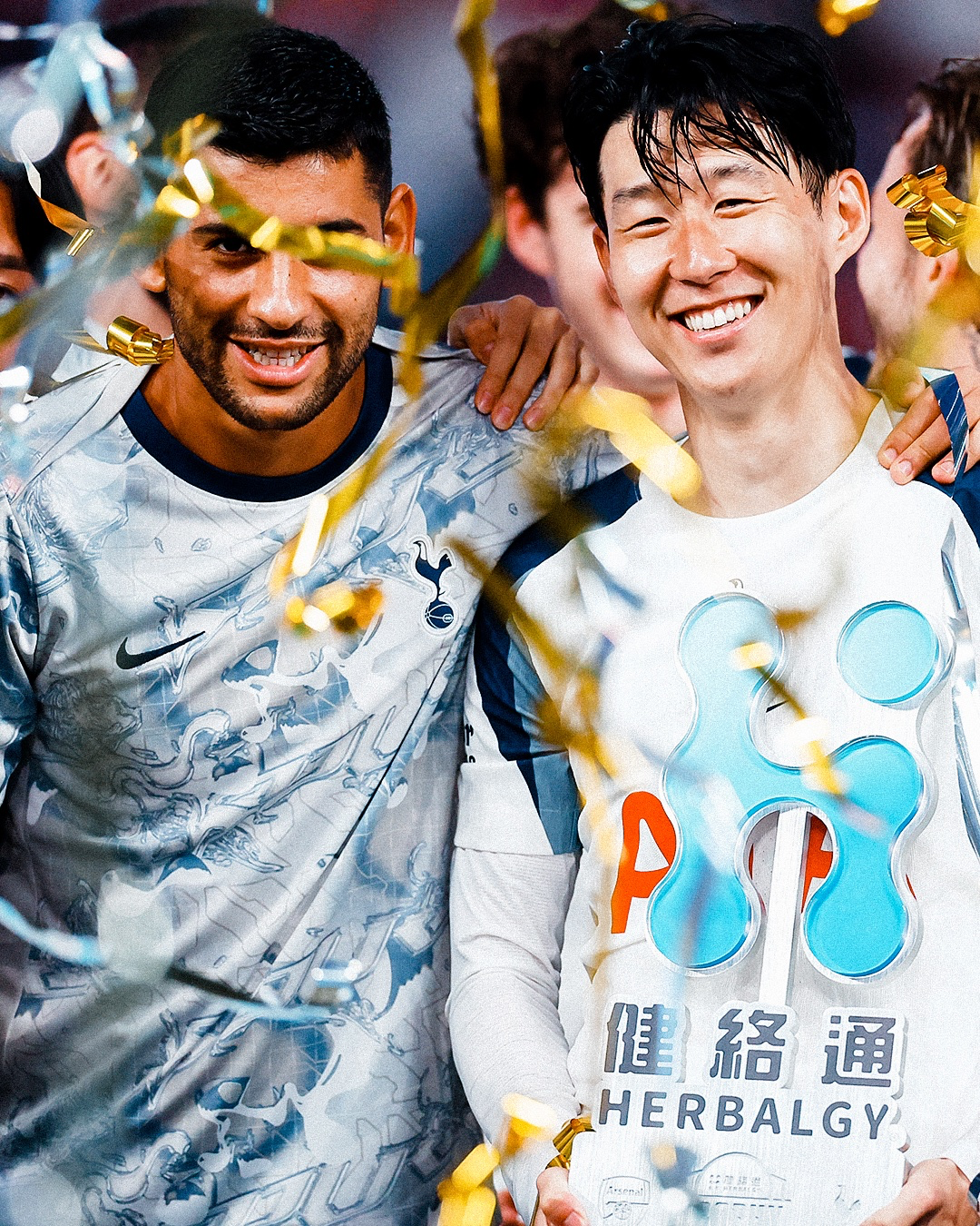 Son Heung-min holds the Herbalgy trophy next to Cuti Romero as gold confetti falls around them.