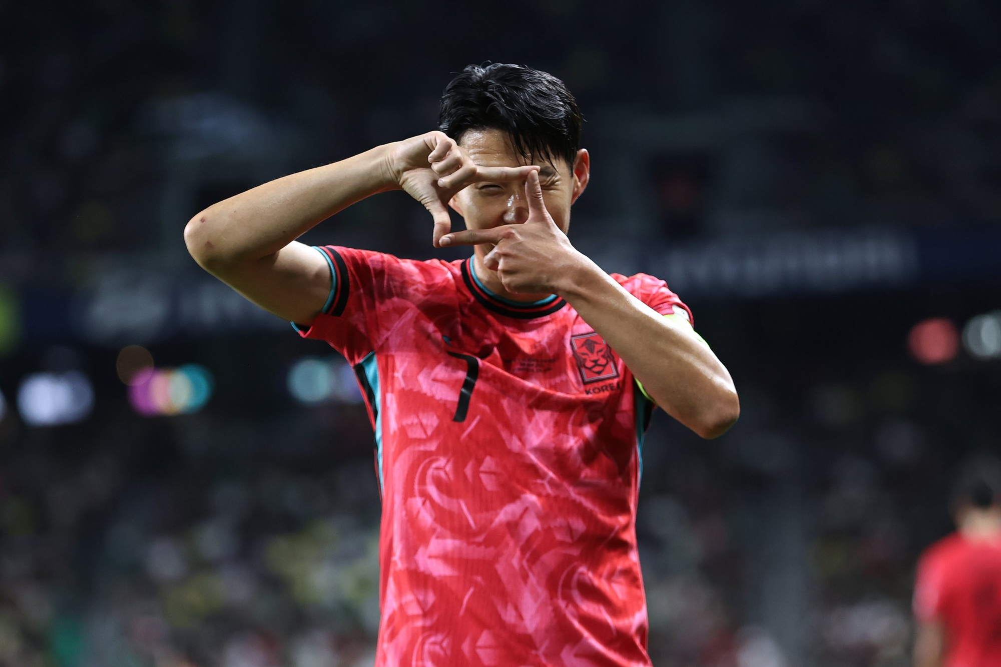 Son Heung-min does his signature camera goal celebration in the South Korea red and pink kit.
