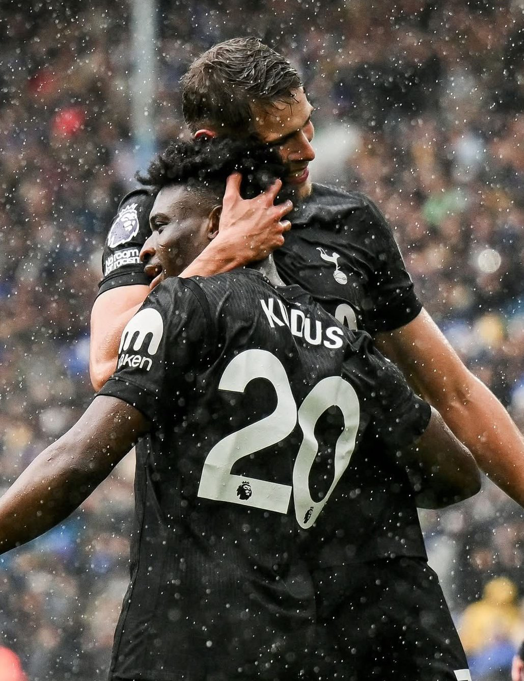 Micky van de Ven draws Mo Kudus in for a hug, rain in the background.