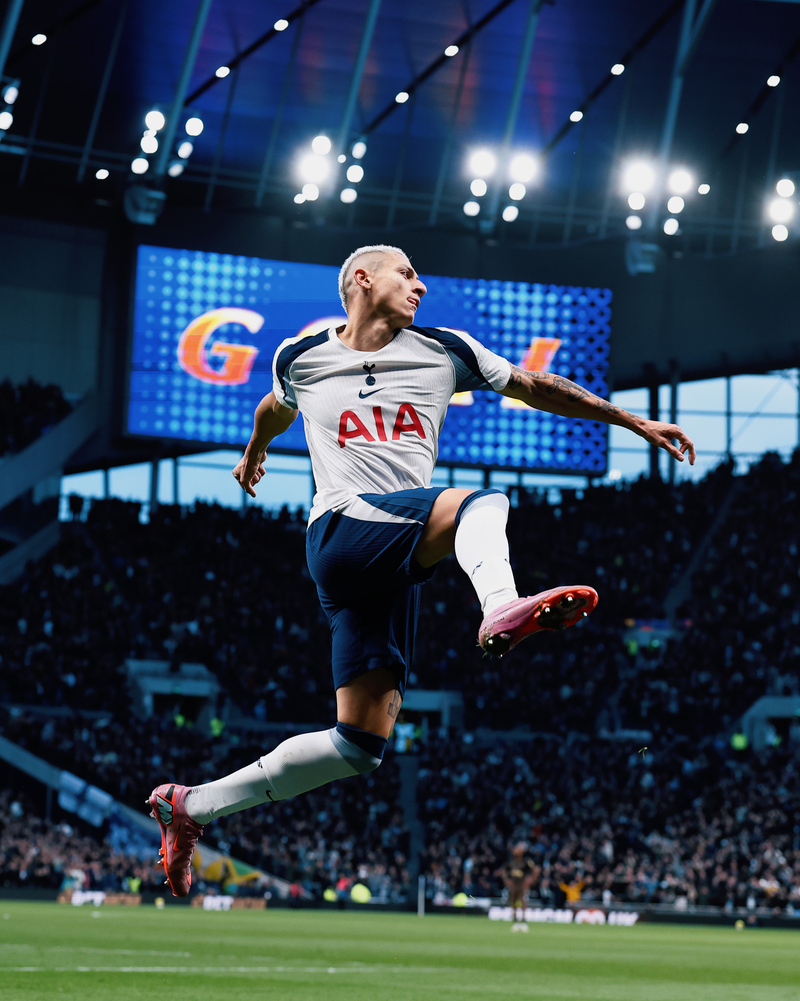 Richarlison leaps into the air in front of the large screen displaying "GOAL" in the background. 