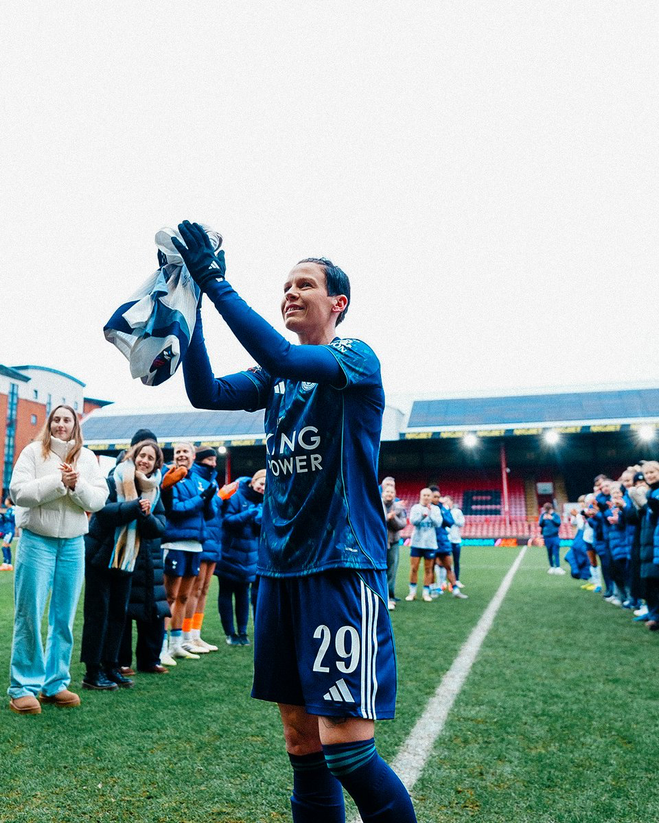 Ash Neville holds up her signed shirt from the team and claps, with the guard of honor behind her.
