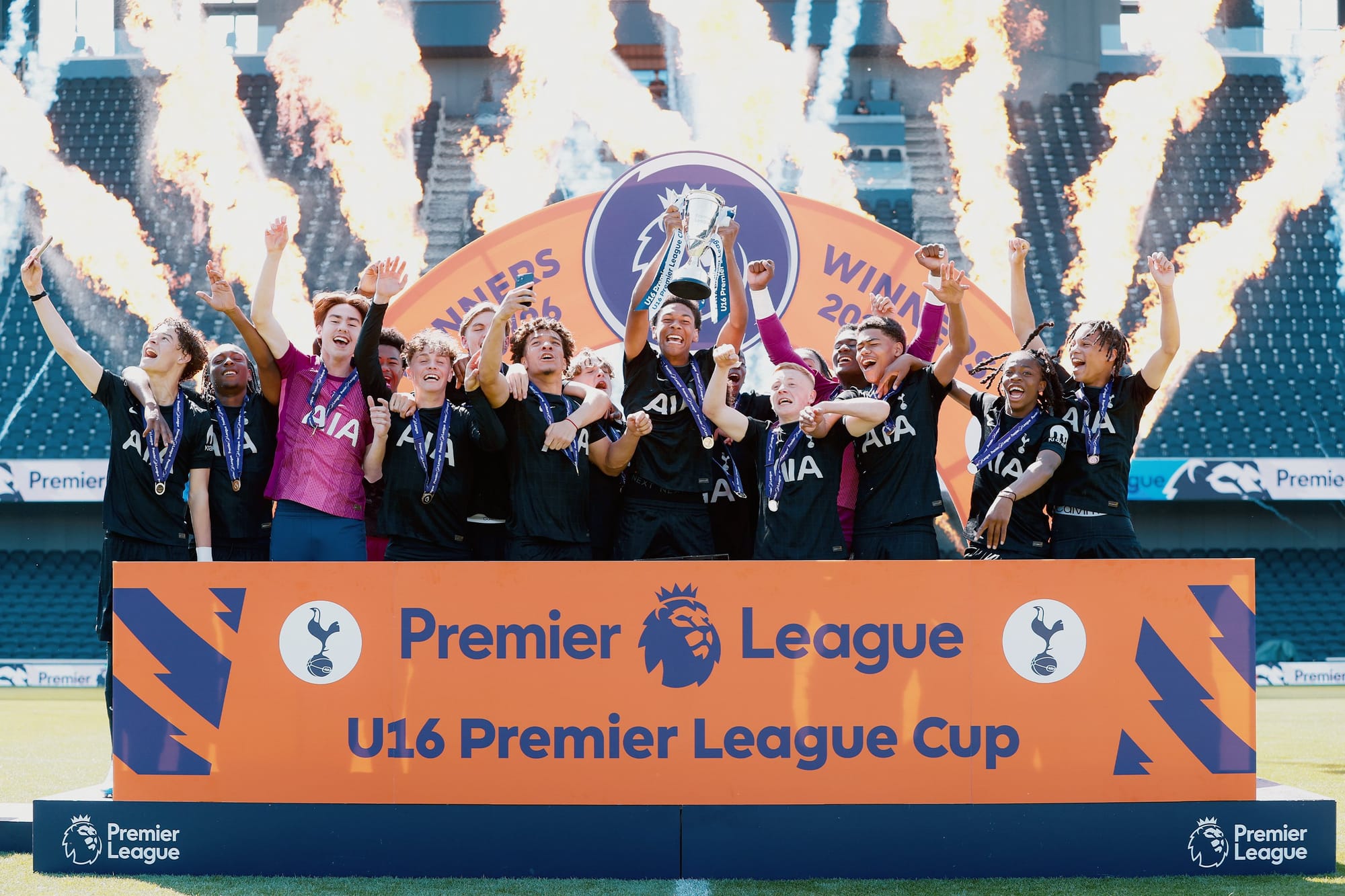 The Men's Academy U16s lift the U16 PL Cup trophy, fireworks behind them.