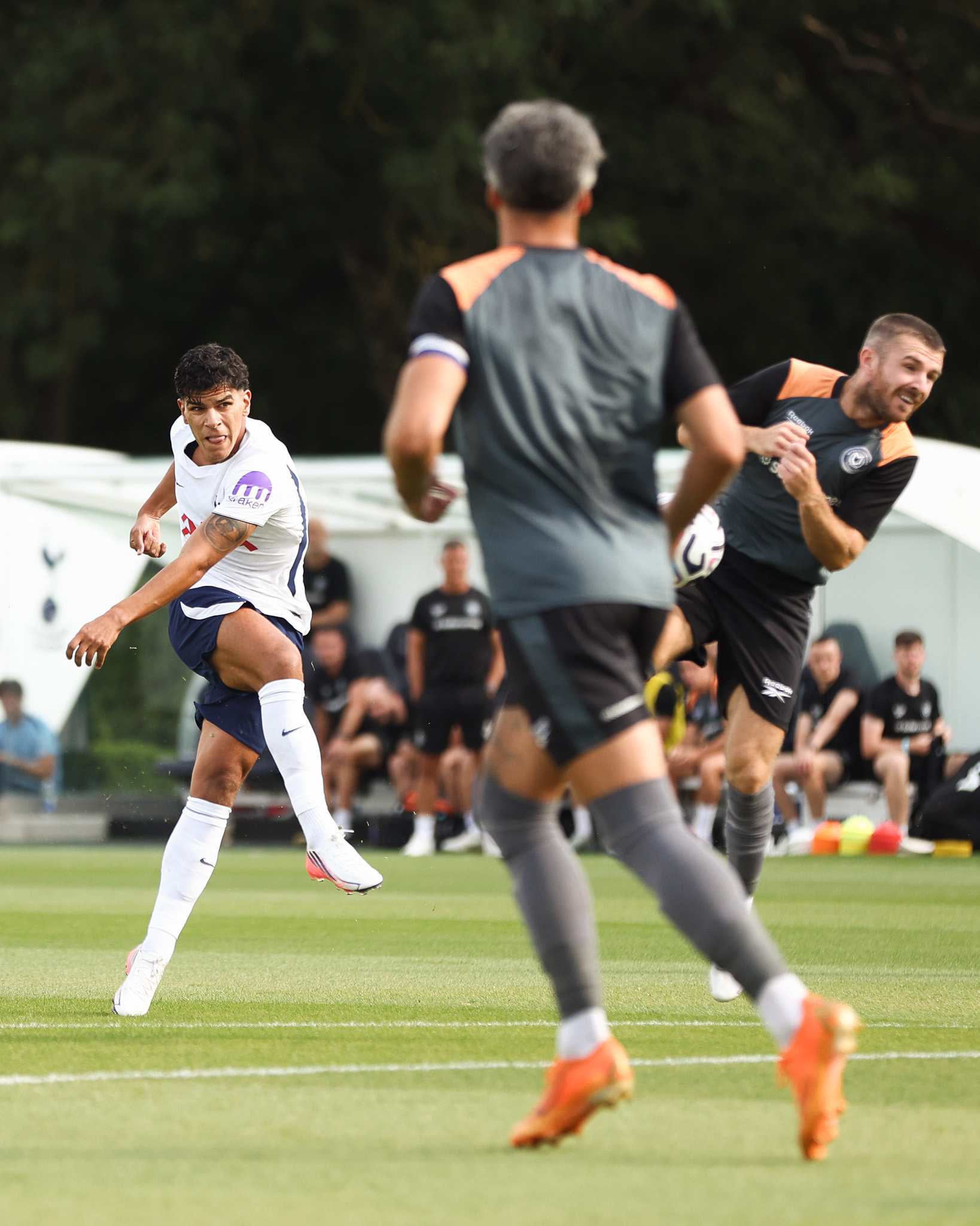 Mateus Fernandes sticks his tongue out as he strikes the ball past several MK Dons players.