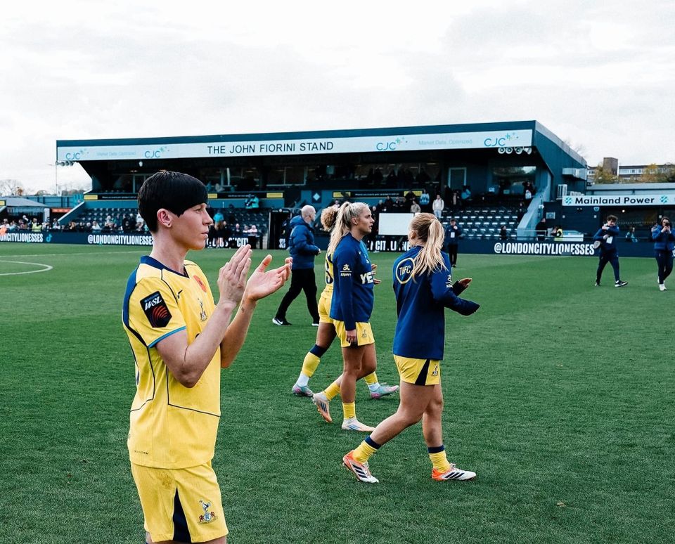 Ash Neville claps the fans after a tough away loss, her teammates in the background.