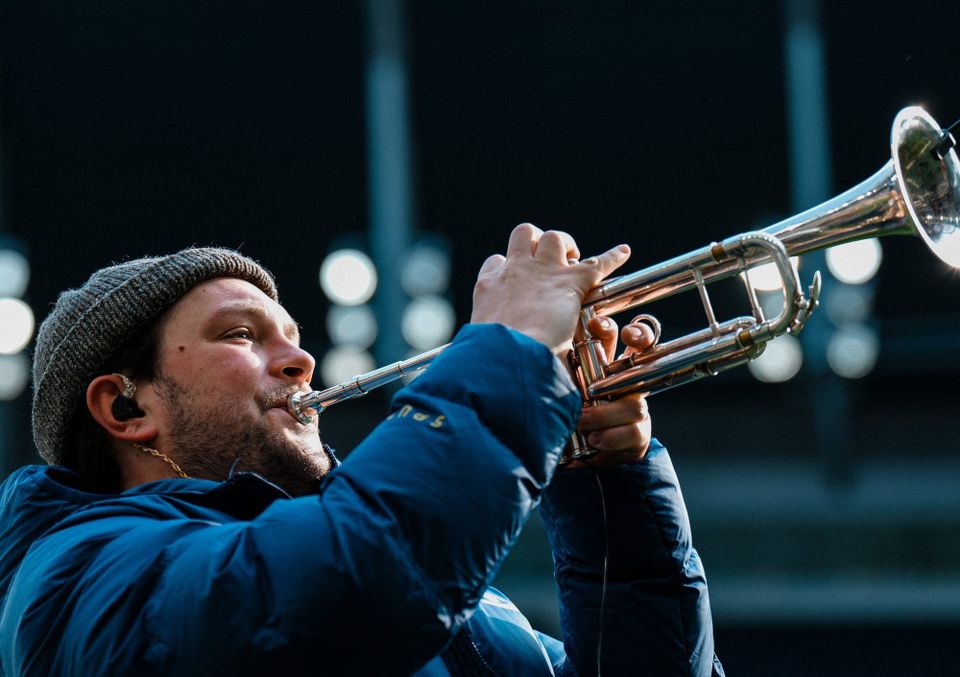 The trumpet player at Tottenham Hotspur Stadium plays his instrument in a beanie hat and puffer.