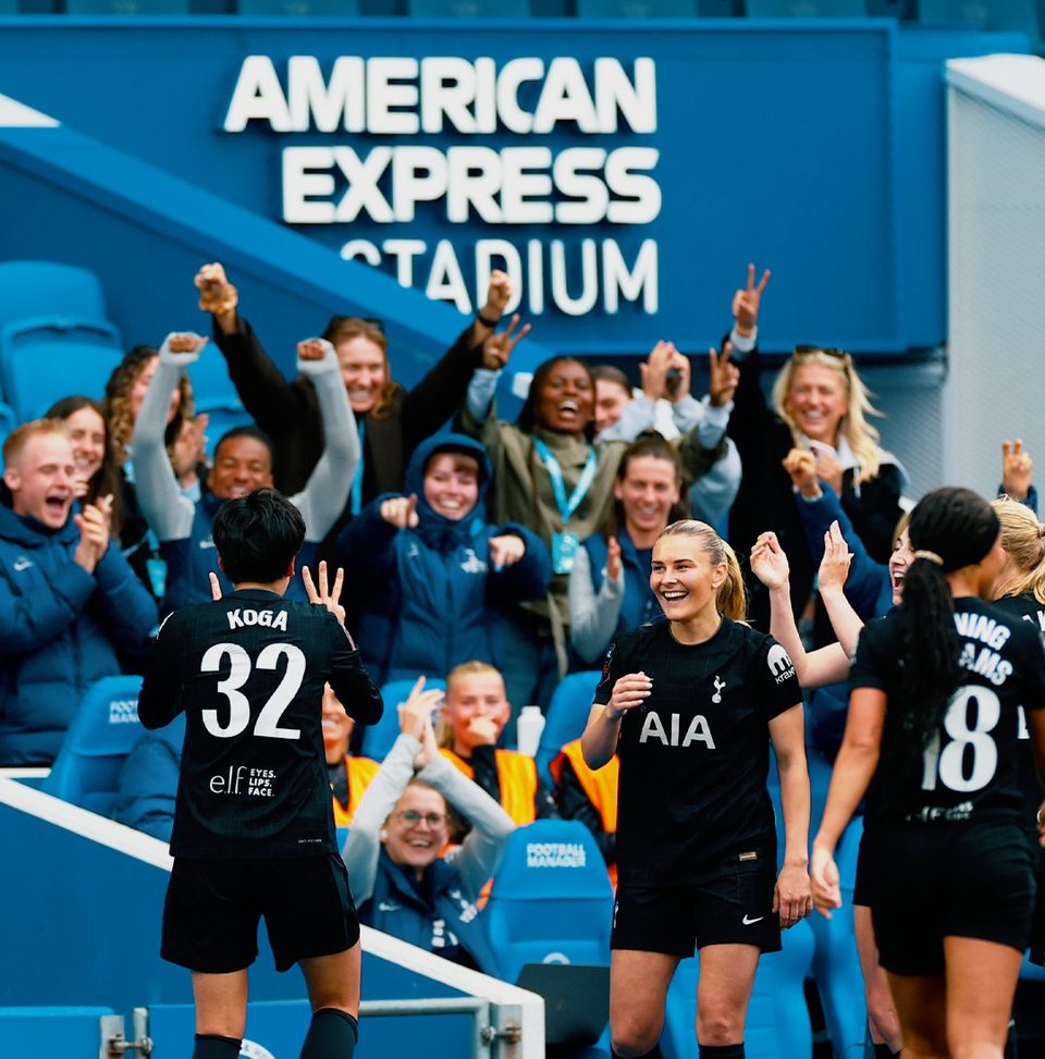 Tōko Koga holds up fingers to represent her kit number, while Amanda Nildén and other teammates smile in the background.