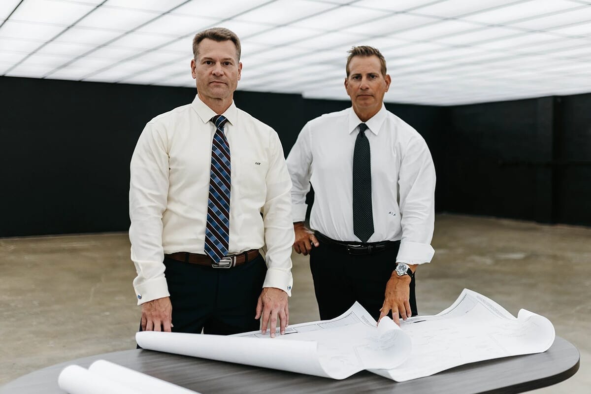 Two men in ties standing over blueprints