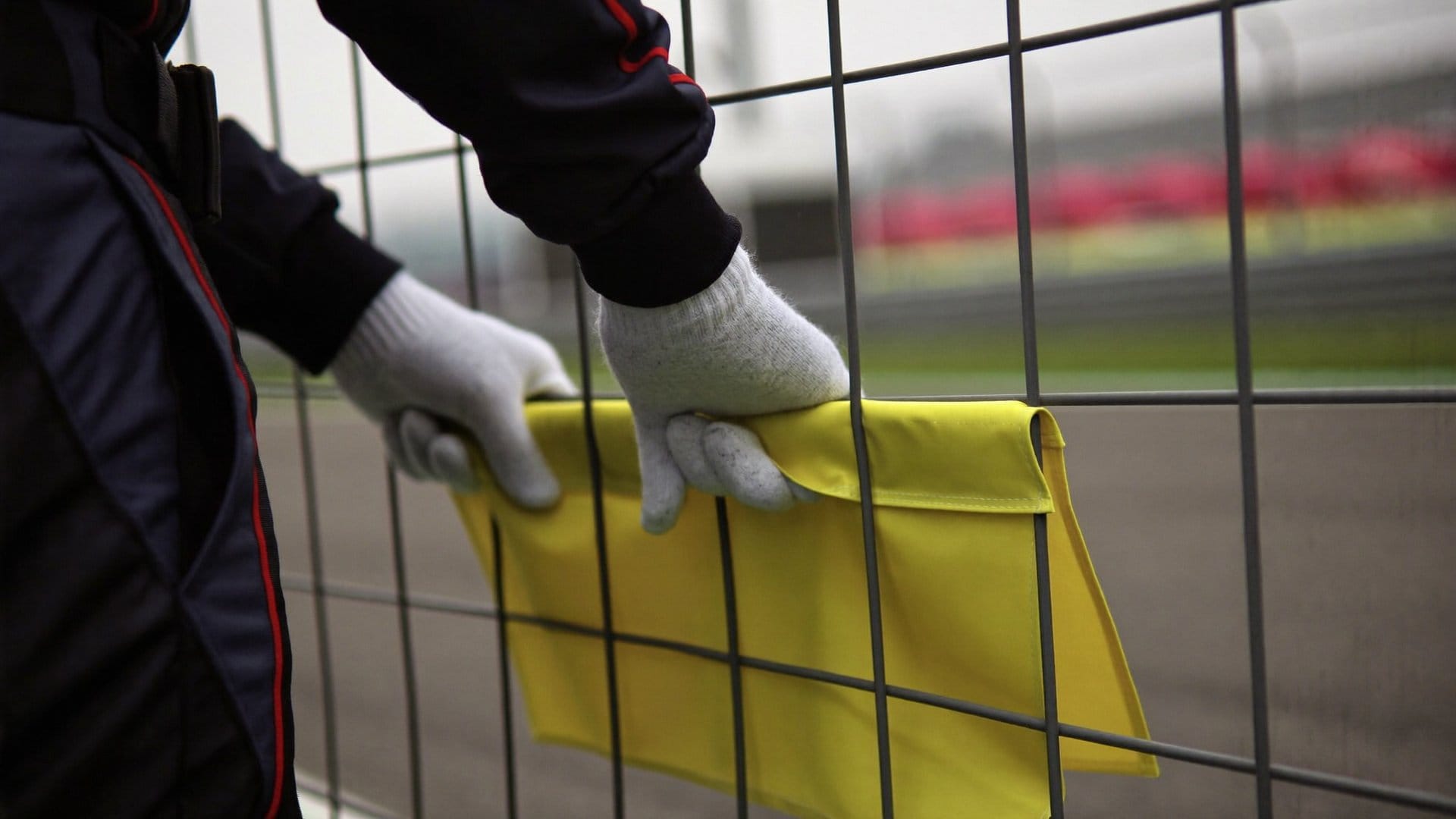 A race marshal holding a folded yellow flag beside a catch fence