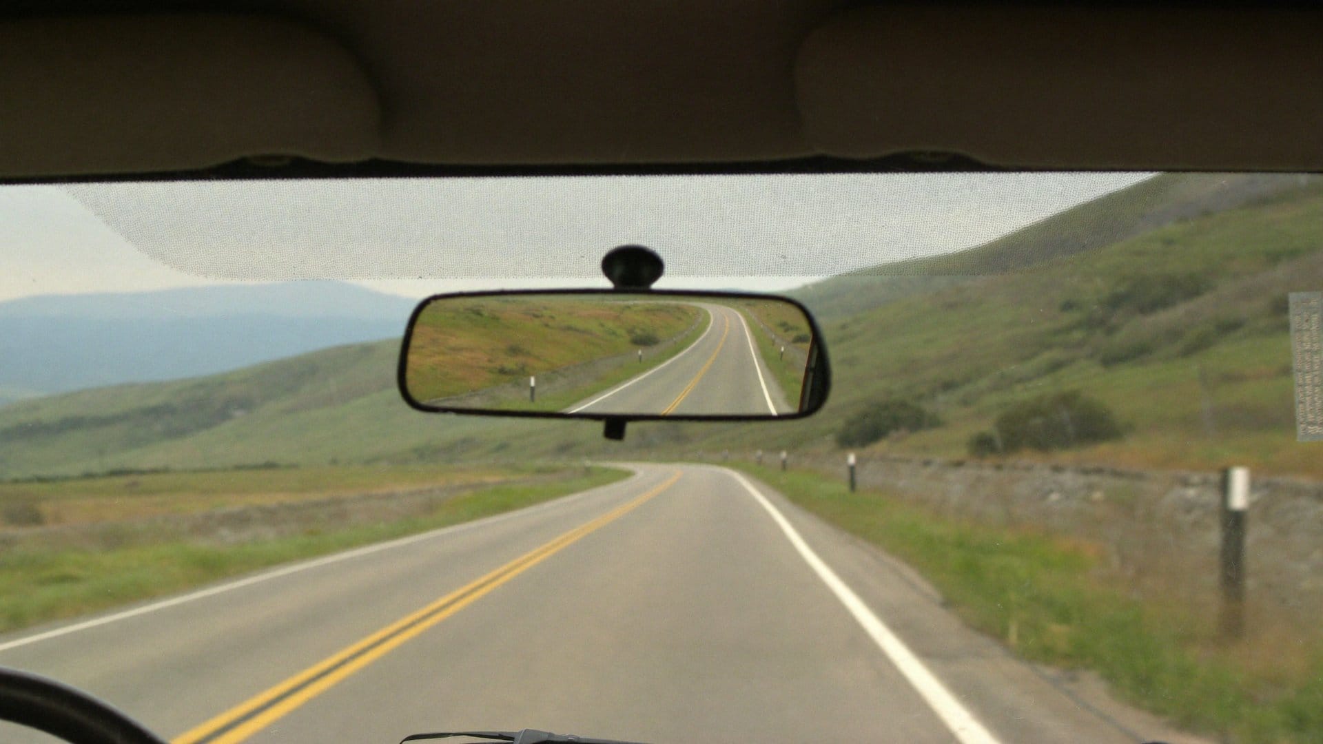 A car rearview mirror reflecting the road behind while an open road lies ahead