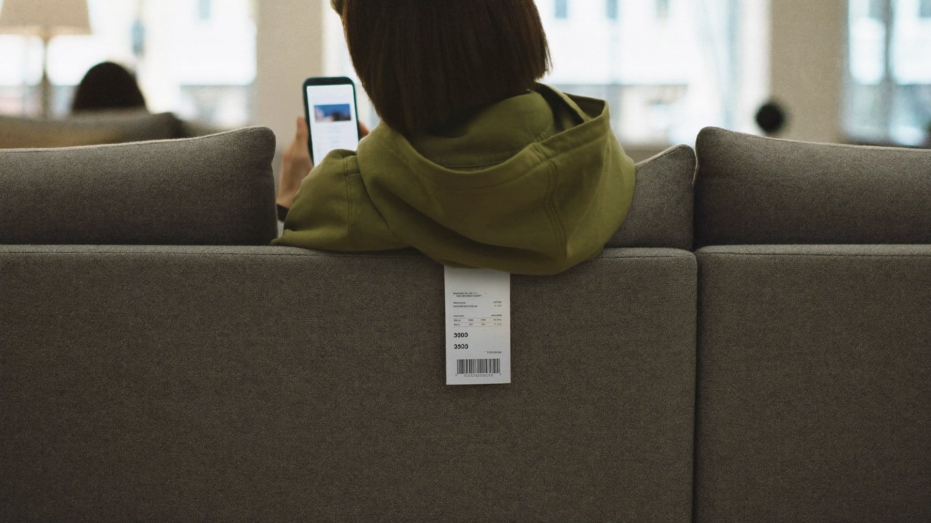 A customer on a showroom sofa comparing the price tag with their phone
