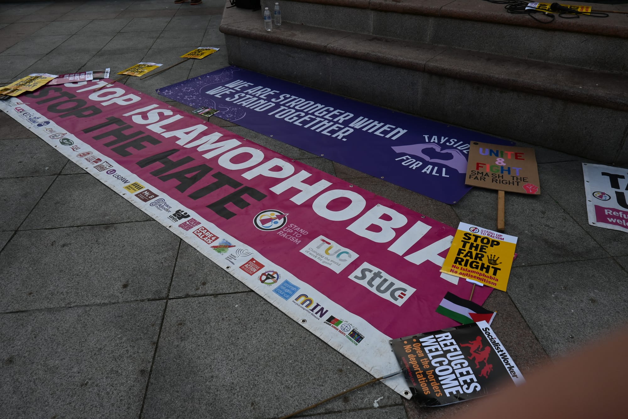 Anti-racism banners and protest signs laid out on pavement, including messages opposing Islamophobia and the far right.