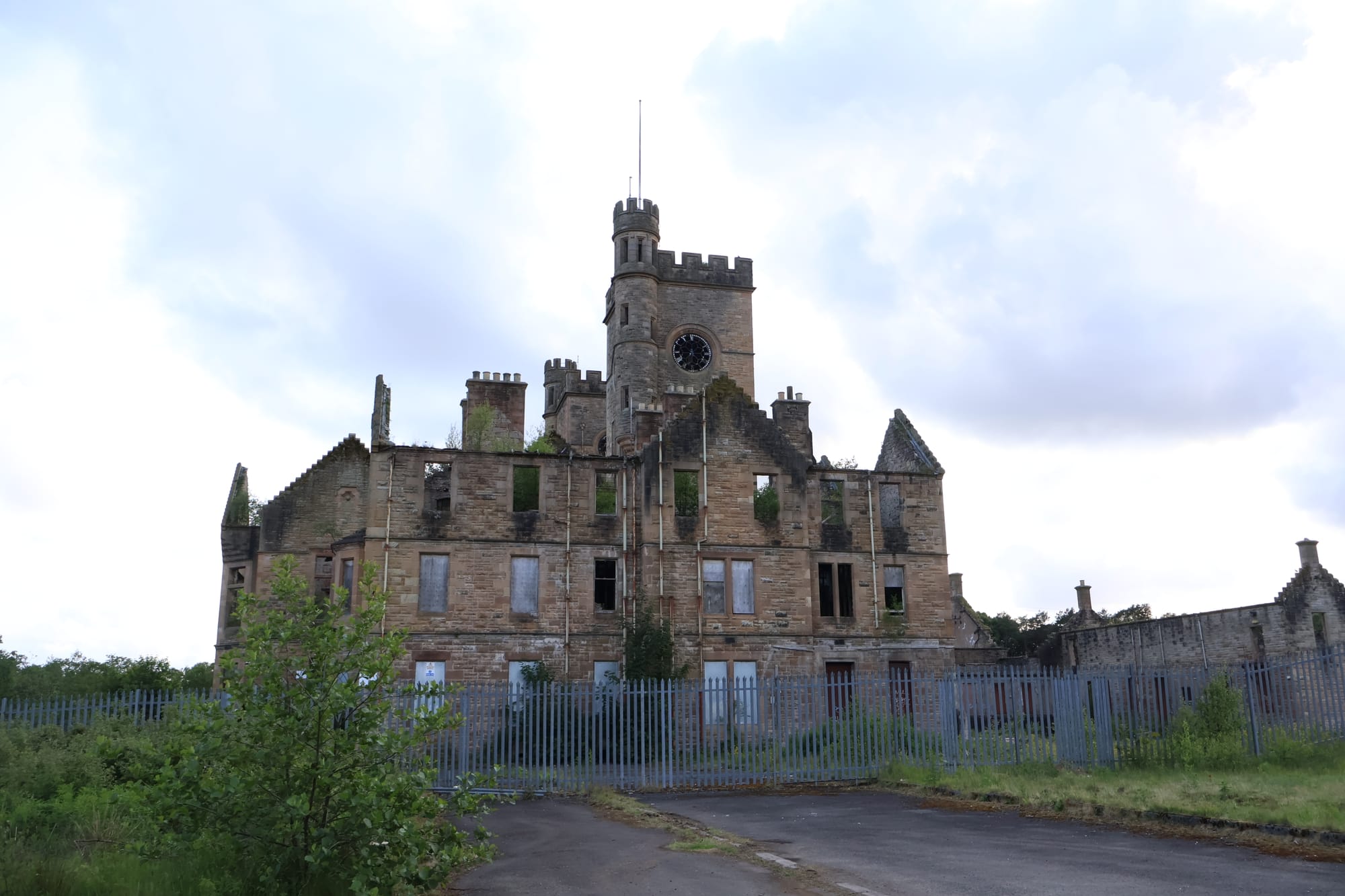 Close-up of the decaying stone exterior of Hartwood Hospital’s nurses’ home, showing broken and boarded windows, weather staining, vegetation and a damaged balcony.