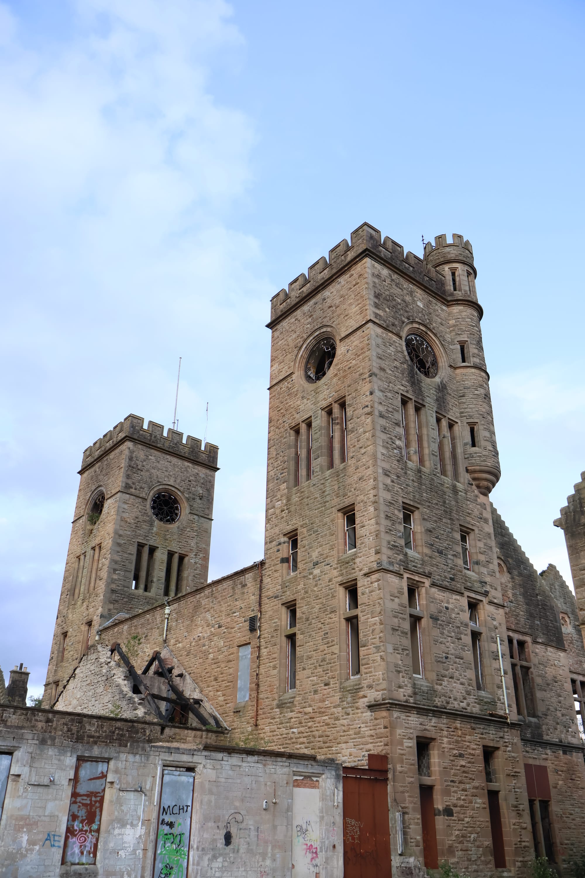 Close-up view of Hartwood Hospital’s two stone clock towers, with broken clock faces, empty windows and damaged sections of the surrounding building.