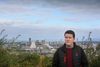 Unite union representative Chris Hamilton standing in a grassy field with Grangemouth refinery’s cooling towers and chimneys