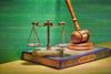 Illustration of a set of brass balance scales resting on an open book titled “Sharia Law,” with a wooden judge’s gavel placed behind them. The background is green.