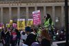Crowd gathered at a protest outside Caird Hall, holding signs reading “Stop the far right” and “Refugees are not to blame,” as a speaker addresses them with a megaphone.