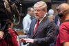 Scottish Government minister Angus Robertson speaking to a television camera during an interview. He is wearing a dark suit and red striped tie, with blurred people visible in the background.