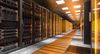 Rows of illuminated server racks line a modern data centre, with glass-fronted cabinets, glowing indicator lights and a brightly lit walkway stretching into the distance.