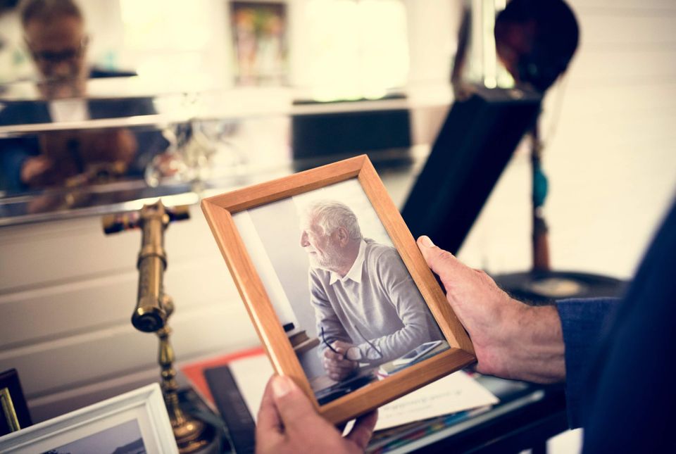 Hands holding a framed photograph of an elderly man sitting alone, deep in thought
