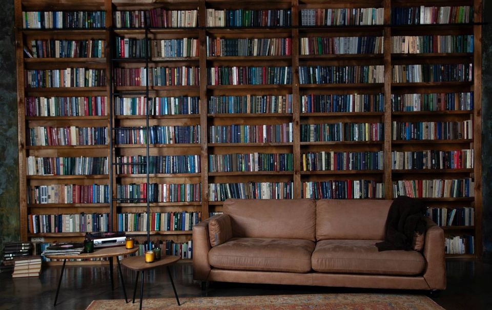 A floor to ceiling personal library with a leather sofa, warm light, and thousands of books on wooden shelves.