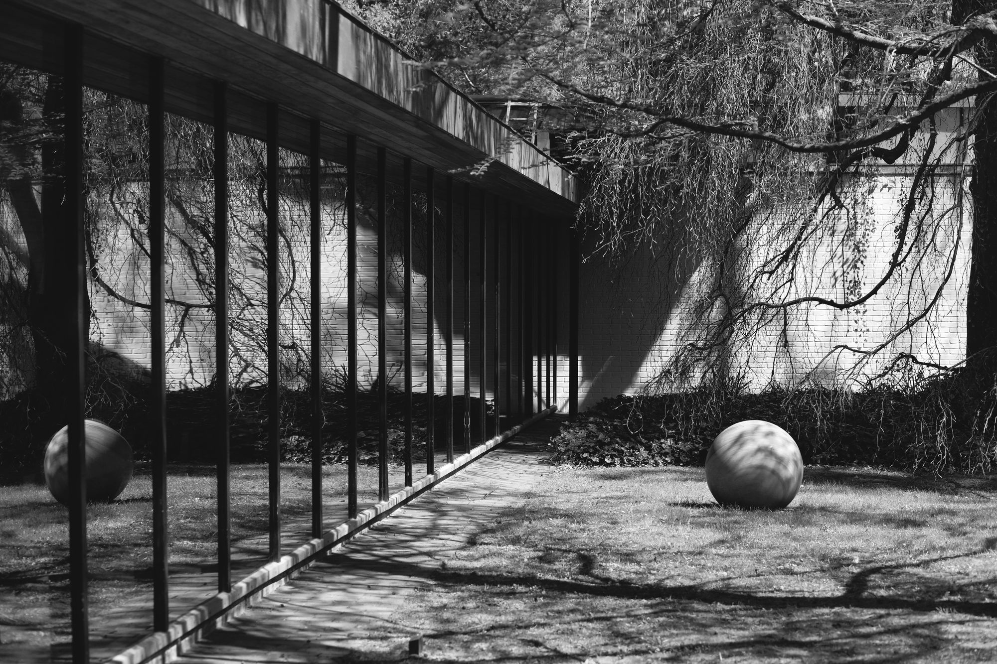 An exterior of the Louisiana Museum of Modern Art, outside Copenhagen. It's a black and white photo of a long glass wall reflecting a large stone sphere resting on the grass.