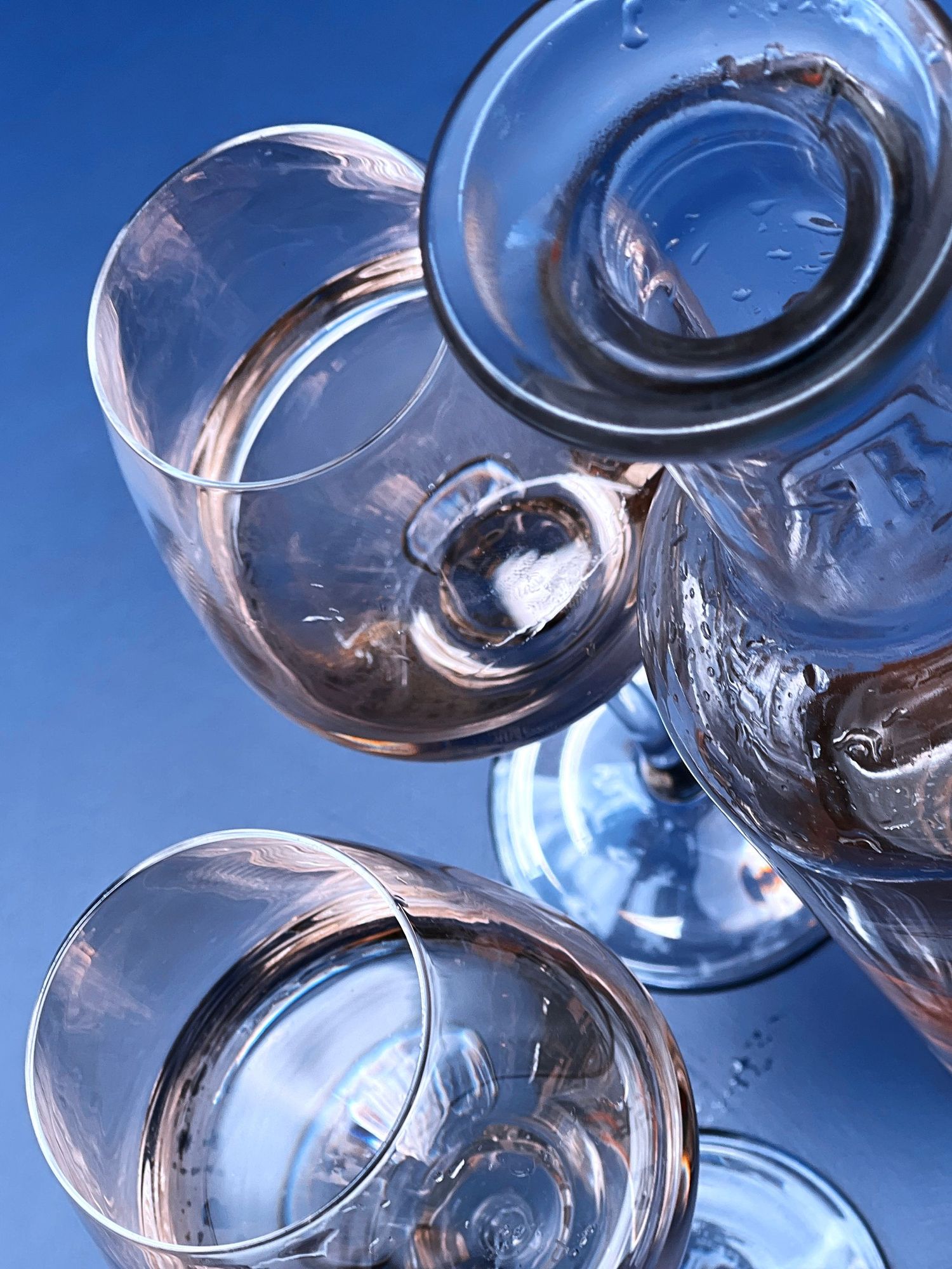 Rose, in wine glasses and a carafe, on a blue table.