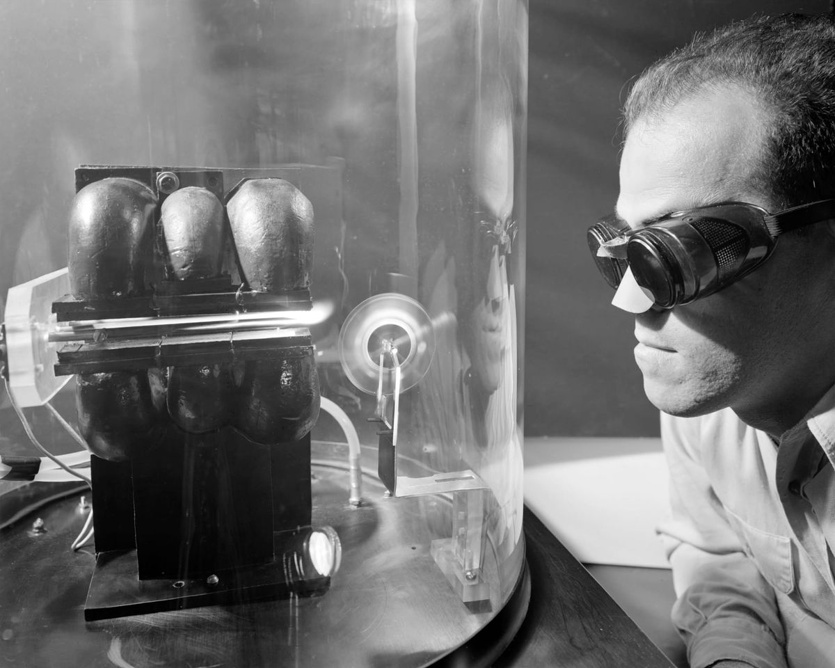 A man wearing safety glasses staring at a small engine-like contraption encased in a plastic tube
