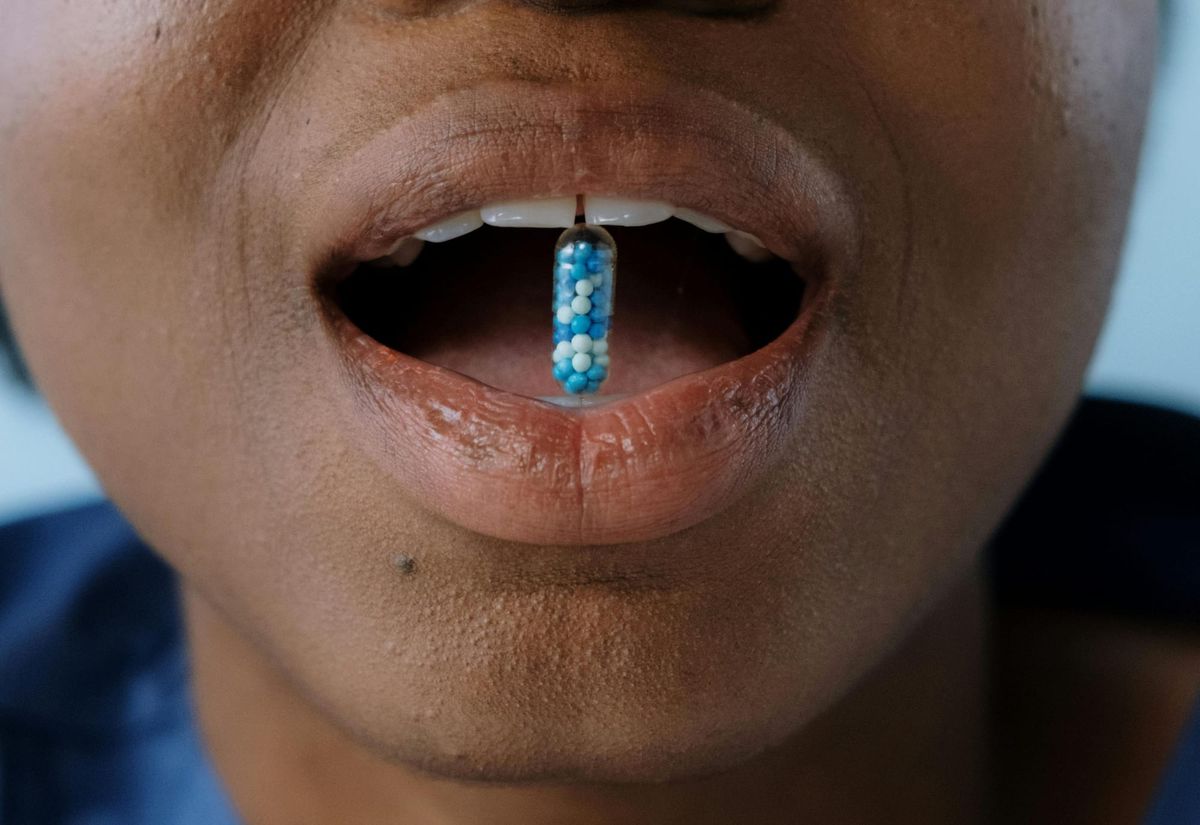 A person holding a pill in their open mouth between their top and bottom teeth