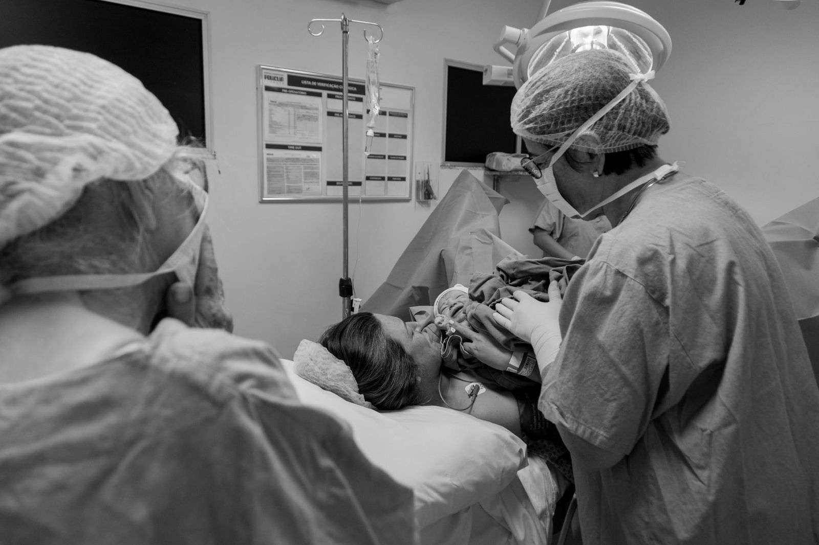 A stock image of a recumbent mother with the newborn in a hospital ward surrounded by medical staff