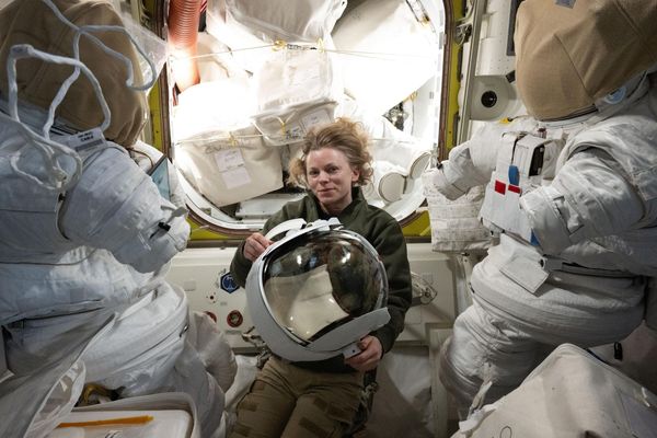 An astronaut floating inside a space station inspects the helmet of a spacesuit