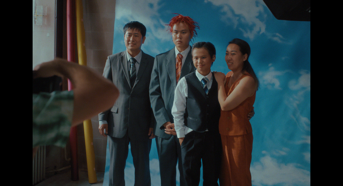 A family poses for a portrait against a painted sky backdrop in Summer School, 2001.