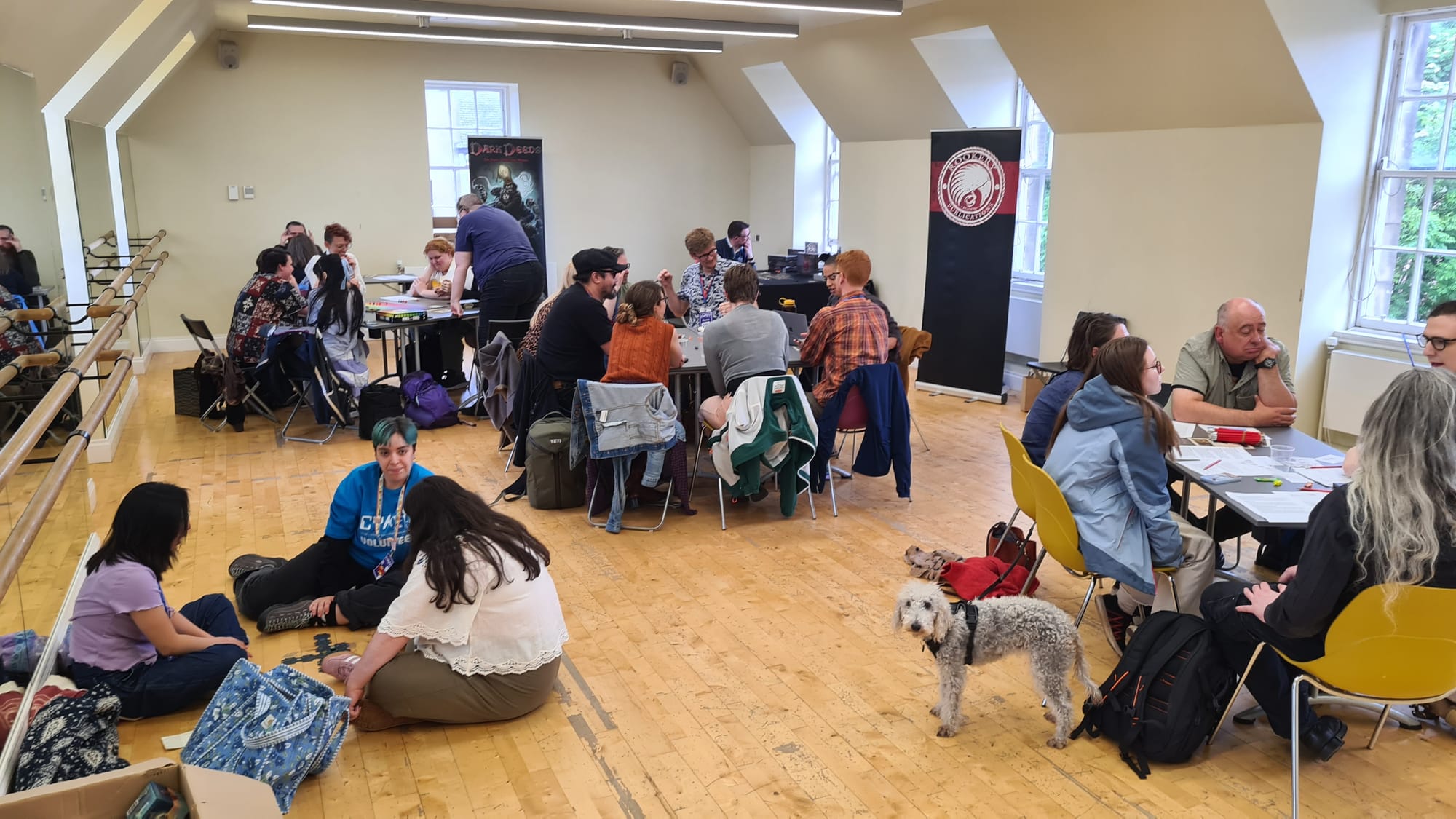 Room full of games players at tables, some seated on floor! Amazing looking Bedlington Terrier pup staring at camera