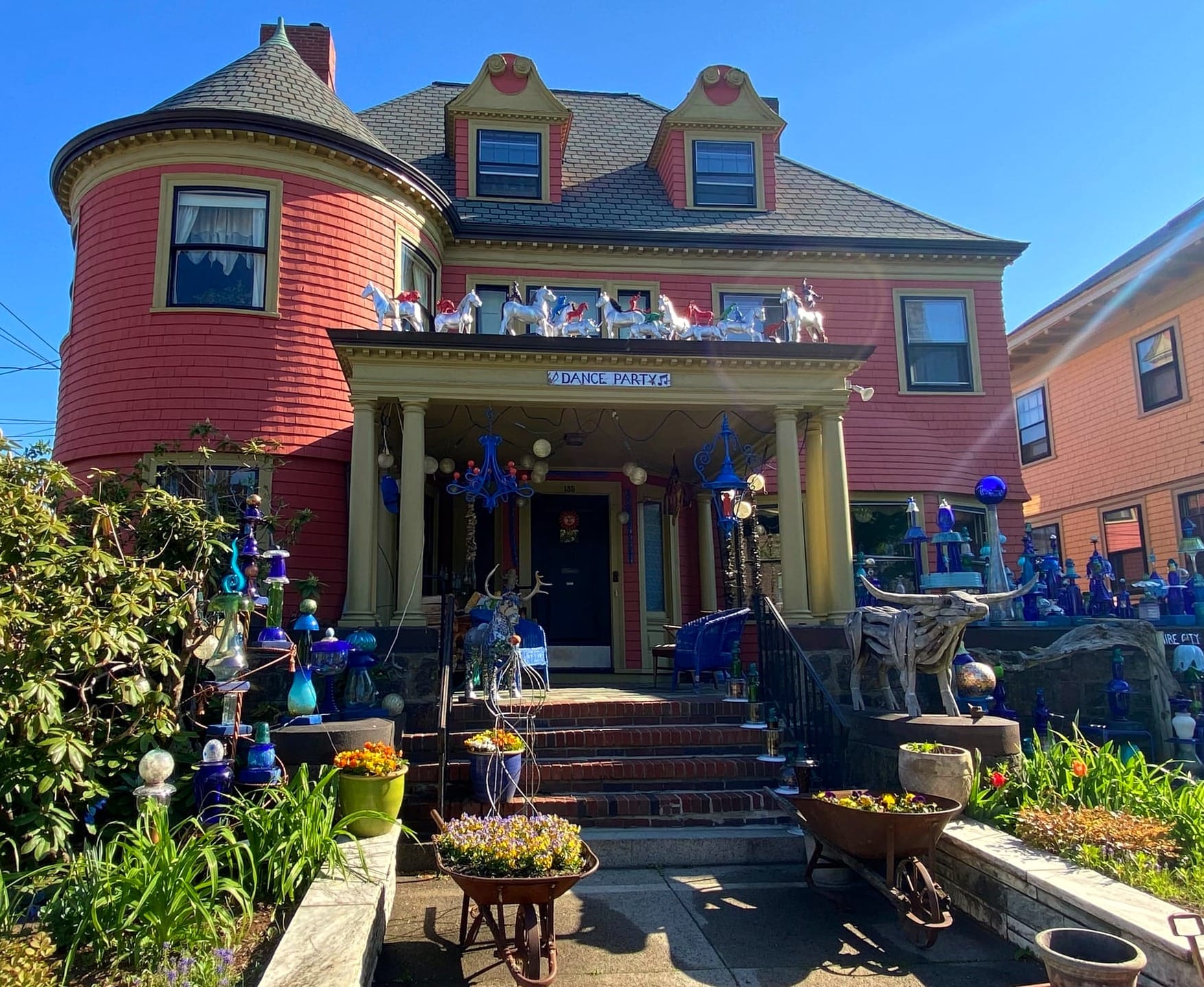 Wide-angle view of the Friend Smithsonian Museum / Blue House / Glass House: three stories; salmon-colored siding; whimsical wooden, glass, and metal sculptures reflect the sun's rays.
