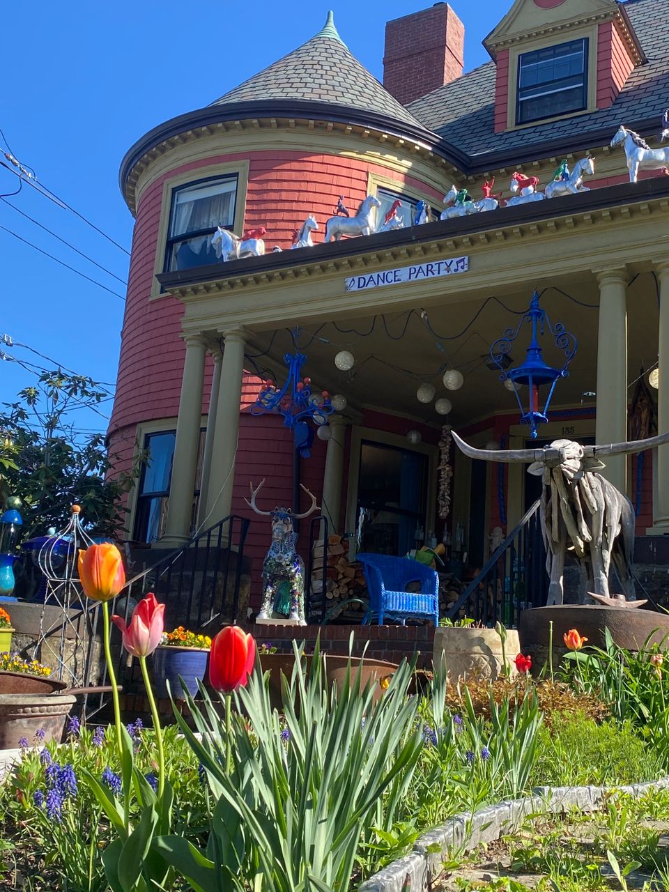 Partial view of the porch of the Friend Smithsonian Museum on a sunny morning. Silver horse statuettes prance on the porch roof. Tulips—red, orange, and pink—bloom in the foreground.