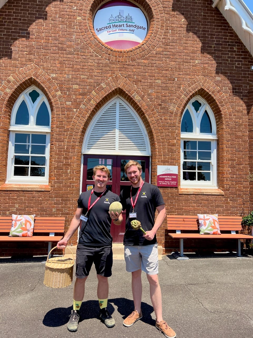 two men in Nutrify shirts holding whole foods in front school building