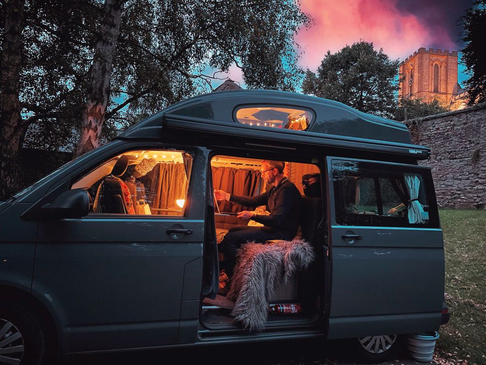 Andy sitting inside Woody, the warmly lit camper van, at dusk