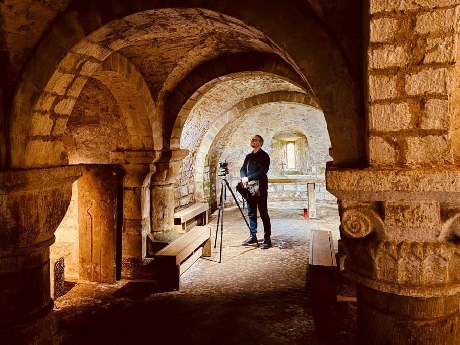 A figure standing within a richly carved Romanesque interior