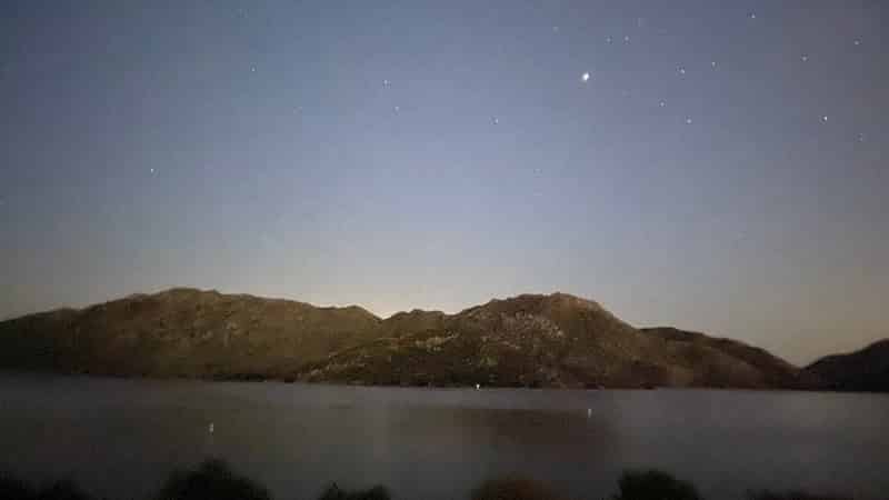 A moody rocky shore across a lake under starlight.