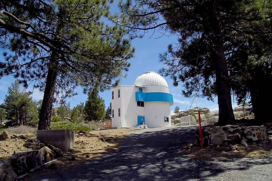 A crisp clean white observatory sits on rock among the pine trees.