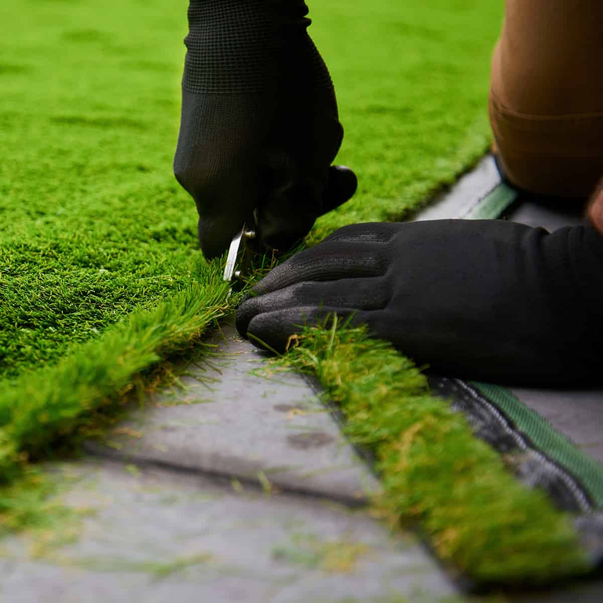 Black-gloved hands of evil fit an artificial lawn into place.