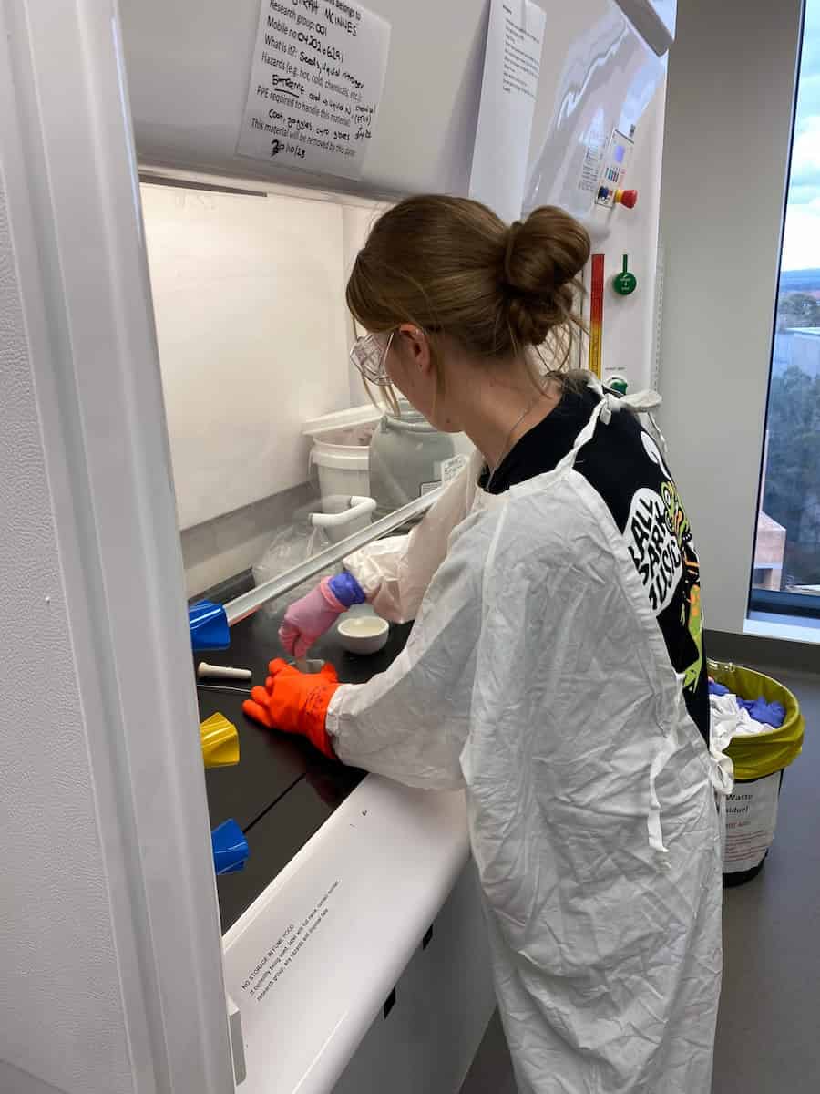 A scientist works on a desk under a fumigated hood. She has her back to camera.
