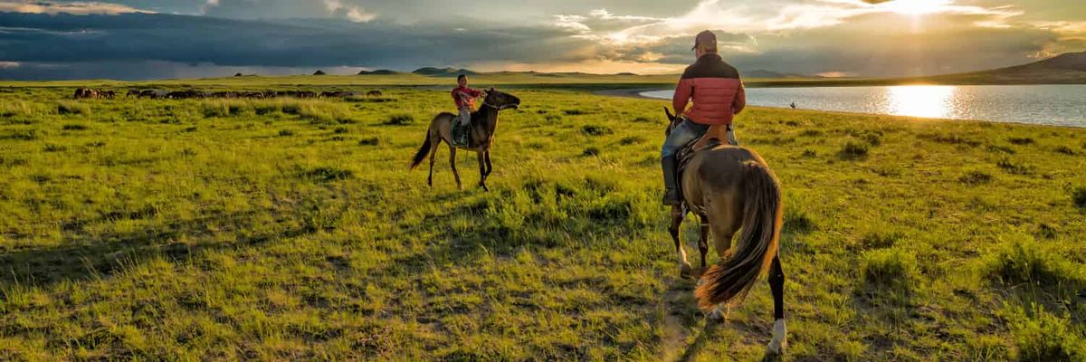 Photo of two people on horseback in the vast and empty Mongolian steppe.