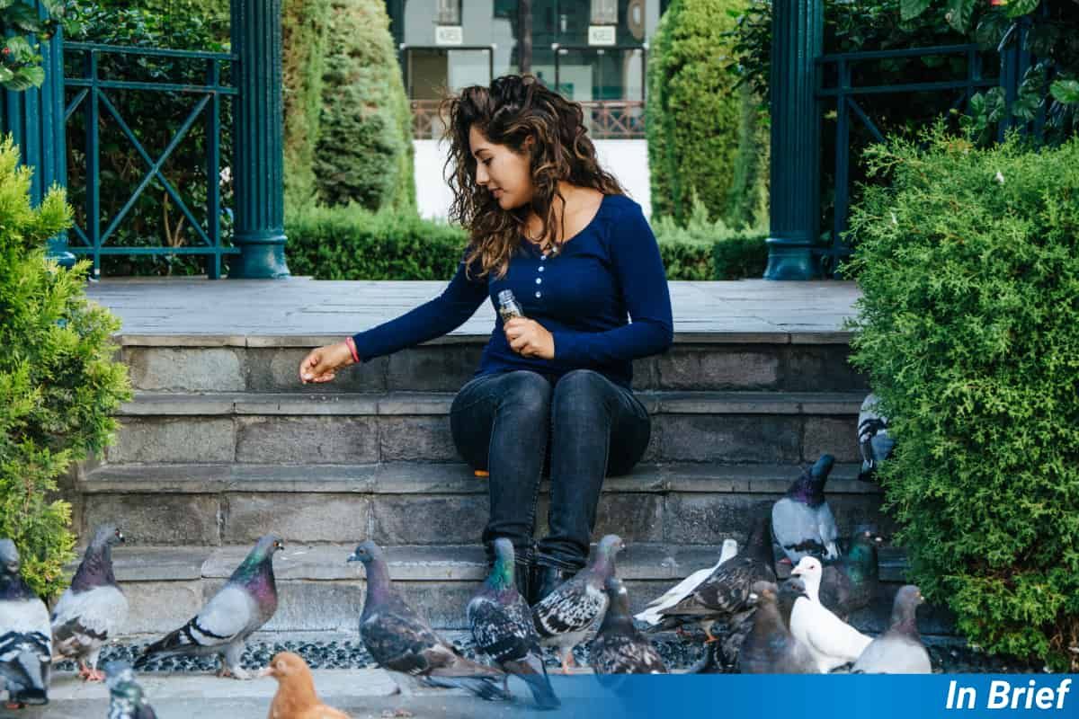 Una mujer alimentando a los pájaros en una ciudad.