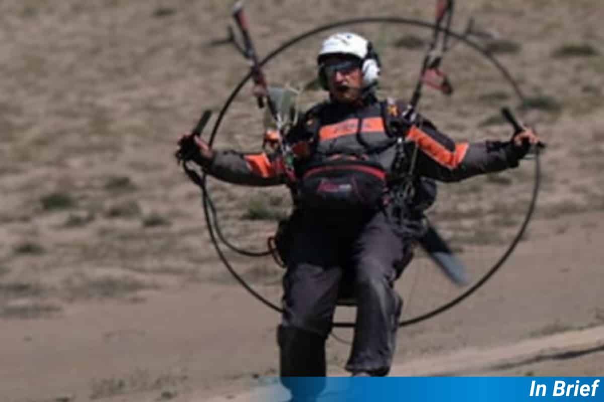 A paraglider pilot lands in a parched landscape.