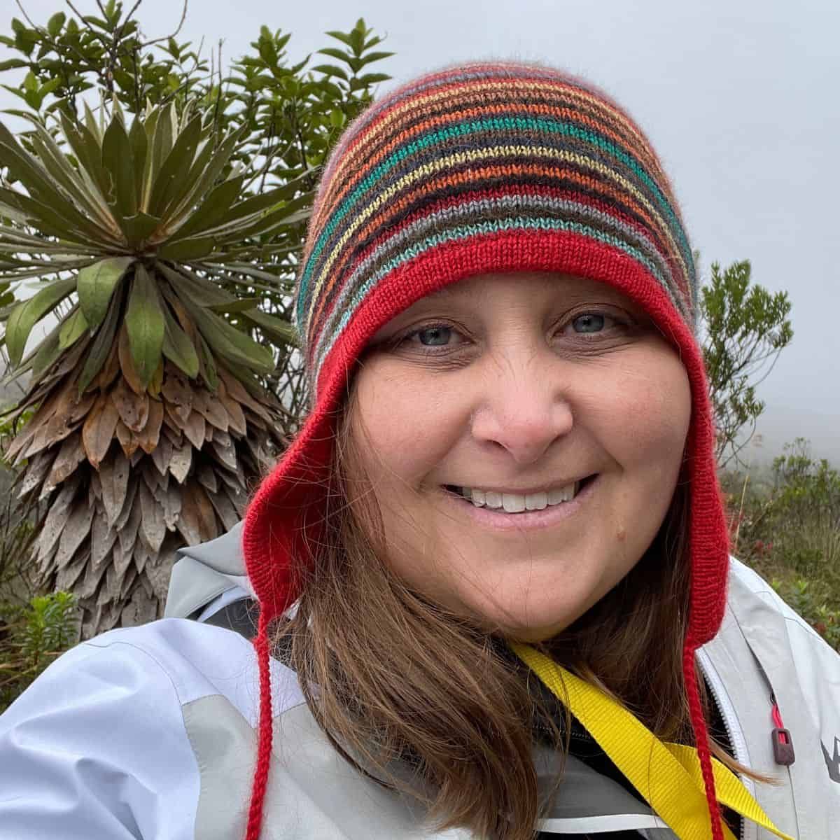 Dr. Laura Lagomarsino smiling at the camera while conducting fieldwork in a tropical environment. She wears a colorful stripe