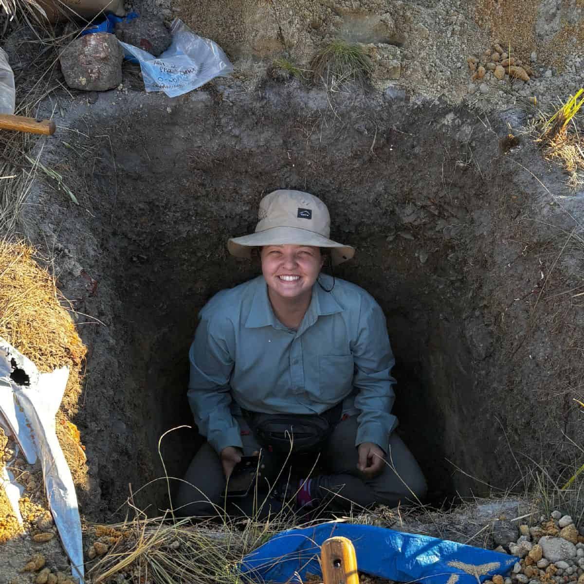A woman in a pit smiling up at the camera.