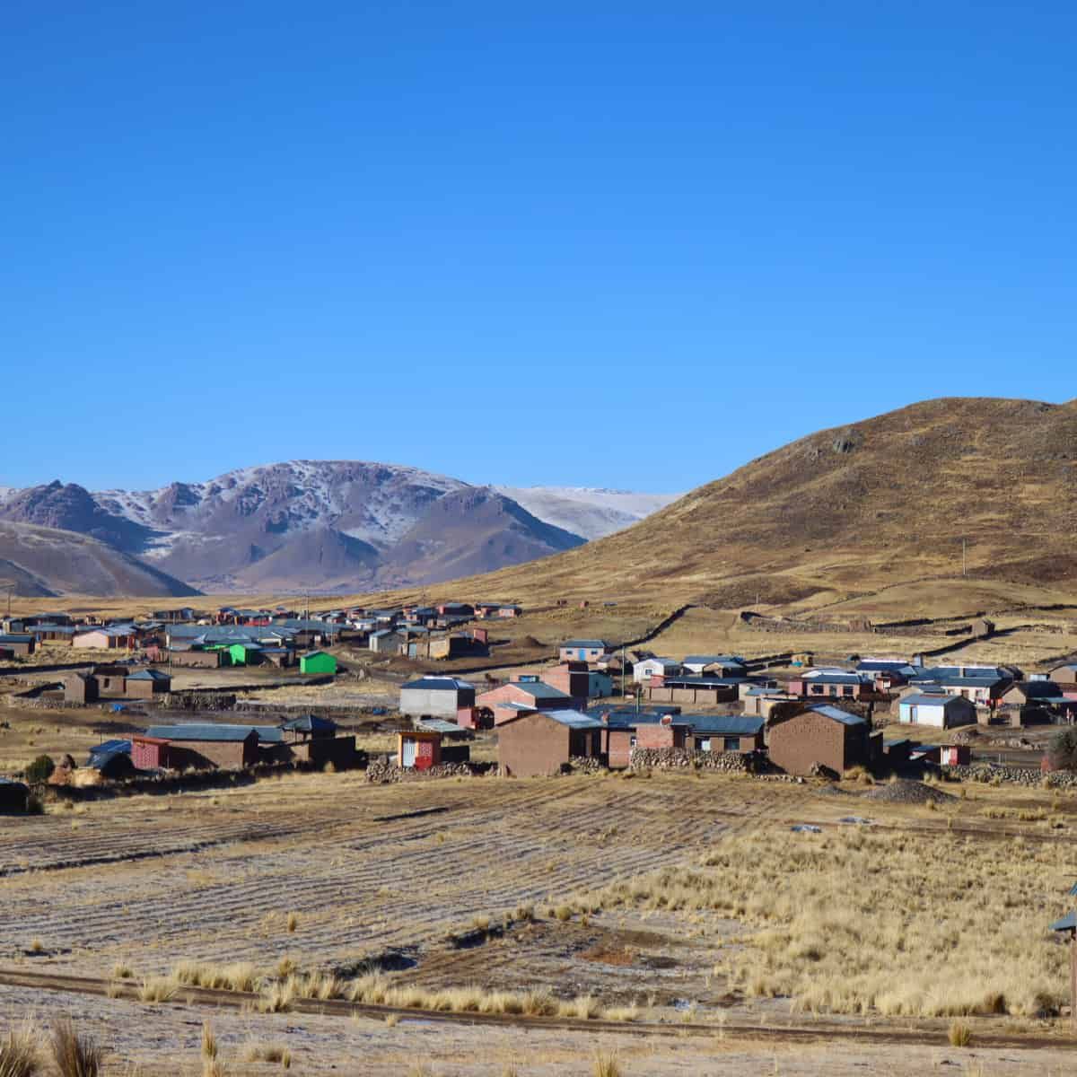View of a contemporary Andean village with colourful houses scattered across high-altitude grassland, with snow-capped mounta