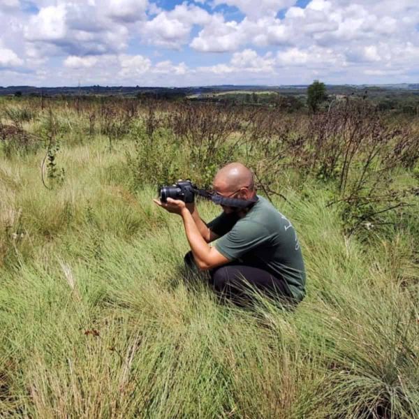 A man squats in thick grassland to take a photograph.