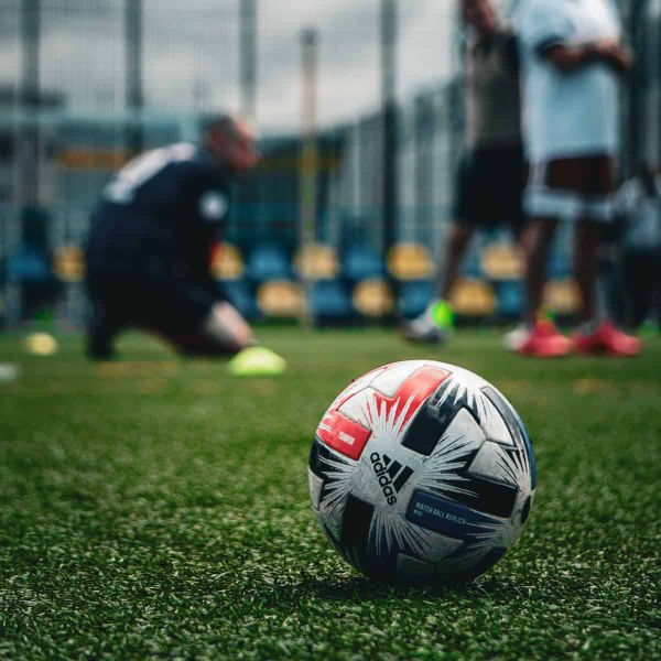 A football in the foreground, with blurred players in the background.