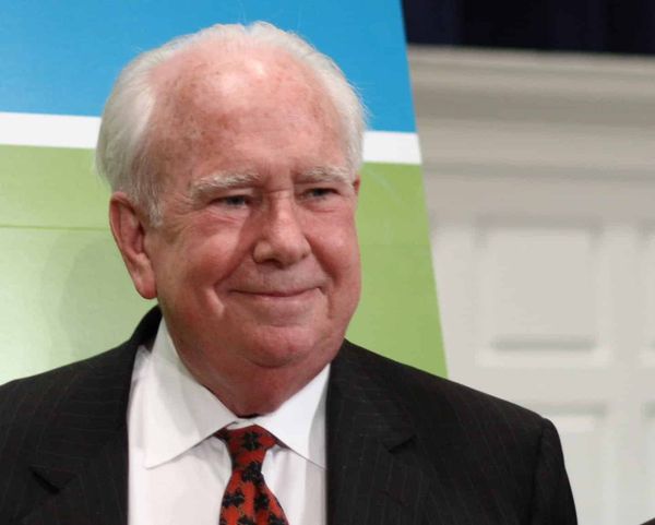 Botanist Peter Raven, white-haired and smiling, in a dark suit and red tie, photographed in 2007.